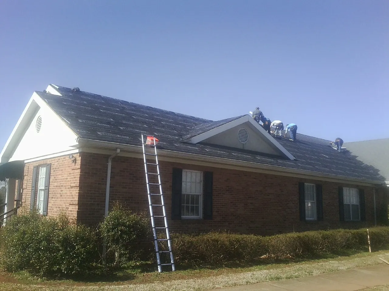 Crew tearing shingles off a brick ranch roof with a ladder set — Emergency Roof Repair work by our crew in Mooreton