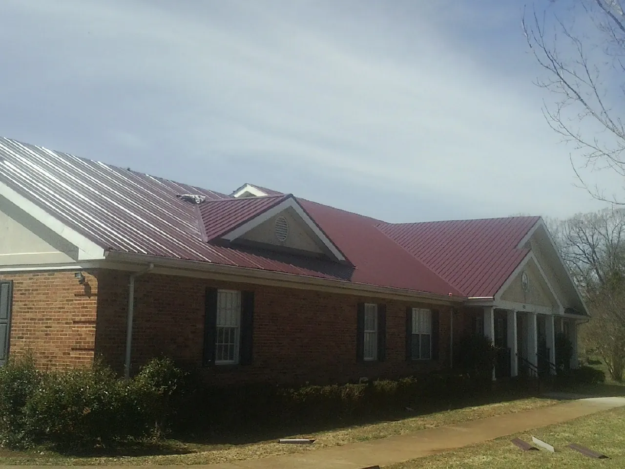 Red metal roof with gabled entries on a long brick building, from a Hail Damage Roof Repair job in Mooreton