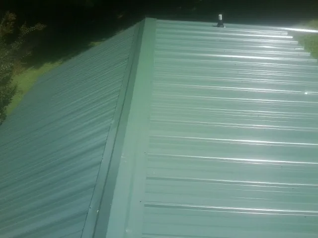 New green metal panels meeting at the ridge of a roof — Flat Roof Repair work by our crew in Mooreton