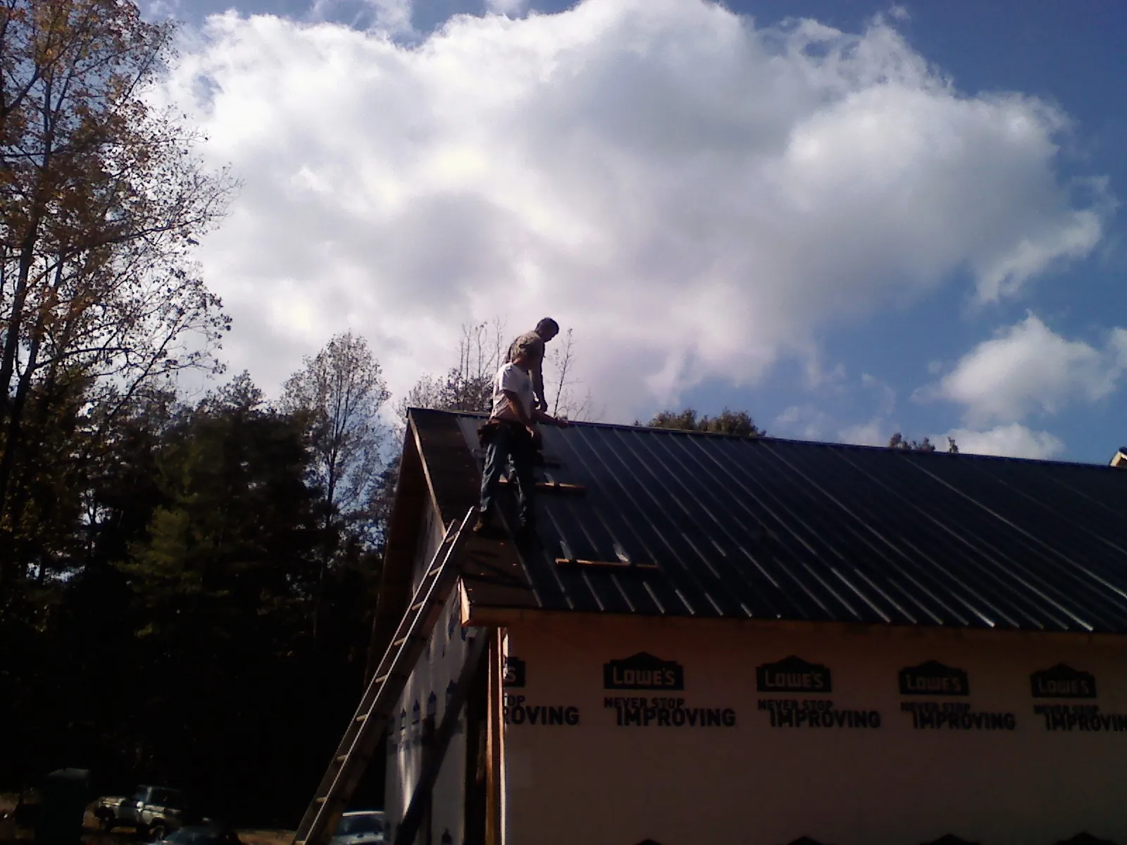Roofer fastening dark metal panels high against a cloudy sky, from a Roof Inspection job in Mooreton