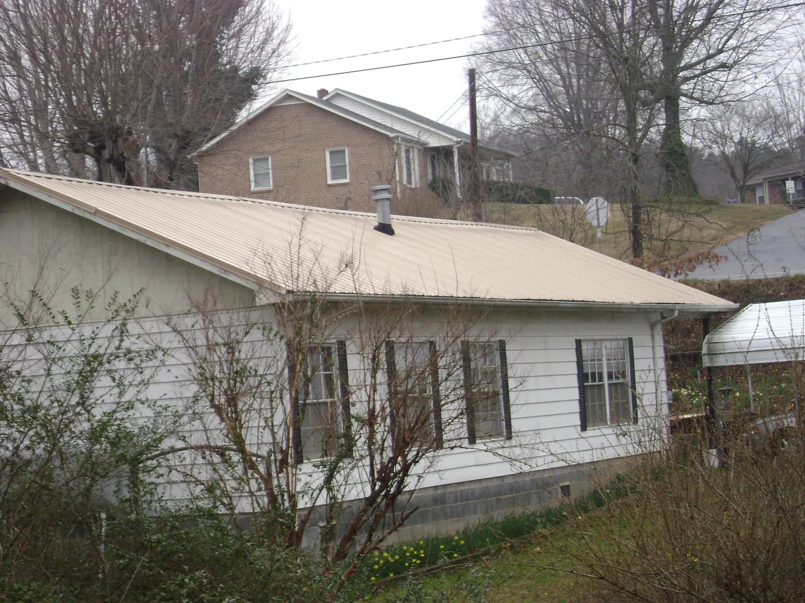 Tan metal roof on a white sided house set into a hillside — Commercial Roofing by Roofing Brothers in Mooreton